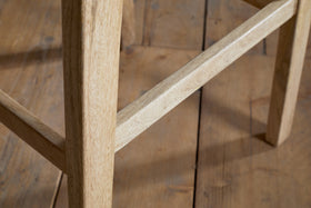 Close-up of the Aamani Mango Wood & Cord Counter Stool - Natural by nkuku, showing its light mango wood legs and support bar set on a rustic wooden floor. The image highlights the stool's smooth finish and natural color.