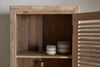 The nkuku Ibo Reclaimed Wood Slatted Tall Cabinet - Natural stands against a beige wall, its slatted door ajar to reveal two small white-and-gray candles on an inner shelf of this rustic storage piece.