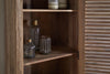 The Ibo Reclaimed Wood Slatted Tall Cabinet by nkuku features a rustic, natural finish and slatted doors. Inside, shelves display clear glass bottles and jars with brass lids, plus two candles in glass holders.