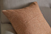 A close-up of the nkuku Ilaa Wool Cushion Cover in Sand, featuring subtle horizontal stripes and a textured, plush look, is displayed on a light beige sofa with a softly woven fabric.