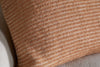 Close-up of the nkuku Ilaa Wool Cushion Cover - Sand, showing its soft brown surface with cream diagonal ribbed stripes. The knitted cover rests against a beige background, emphasizing its cozy material and warm, earthy tones.