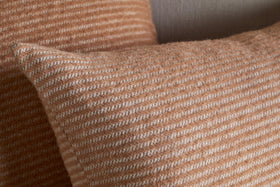 Close-up of two nkuku Ilaa Wool Cushion Covers in Sand. The soft, rectangular covers have textured, fuzzy wool with thin, horizontal cream and light brown stripes for a cozy look against a neutral, blurred background.