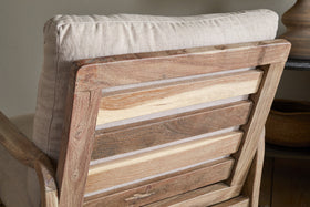 Close-up of the nkuku Jaya Acacia Wood & Linen Occasional Chair – Natural, highlighting its varied-tone horizontal acacia slats and light linen back cushion. The design creates a rustic, cozy atmosphere.