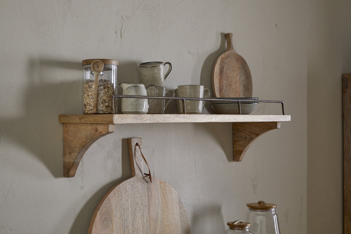 The nkuku Meera Mango Wood & Iron Gallery Shelf in Natural displays a glass jar with oats, ceramic cups, a creamer, and a tray. Below, two round cutting boards hang on the wall for rustic kitchen storage in neutral tones.