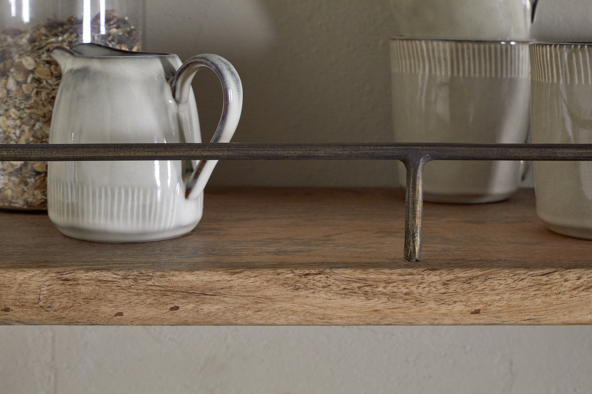 A close-up of the nkuku Meera Mango Wood & Iron Gallery Shelf – Natural, displaying an off-white ceramic pitcher and two cups with subtle gray accents, plus a jar of oats. A dark iron rail provides stylish support to this elegant kitchen storage piece.