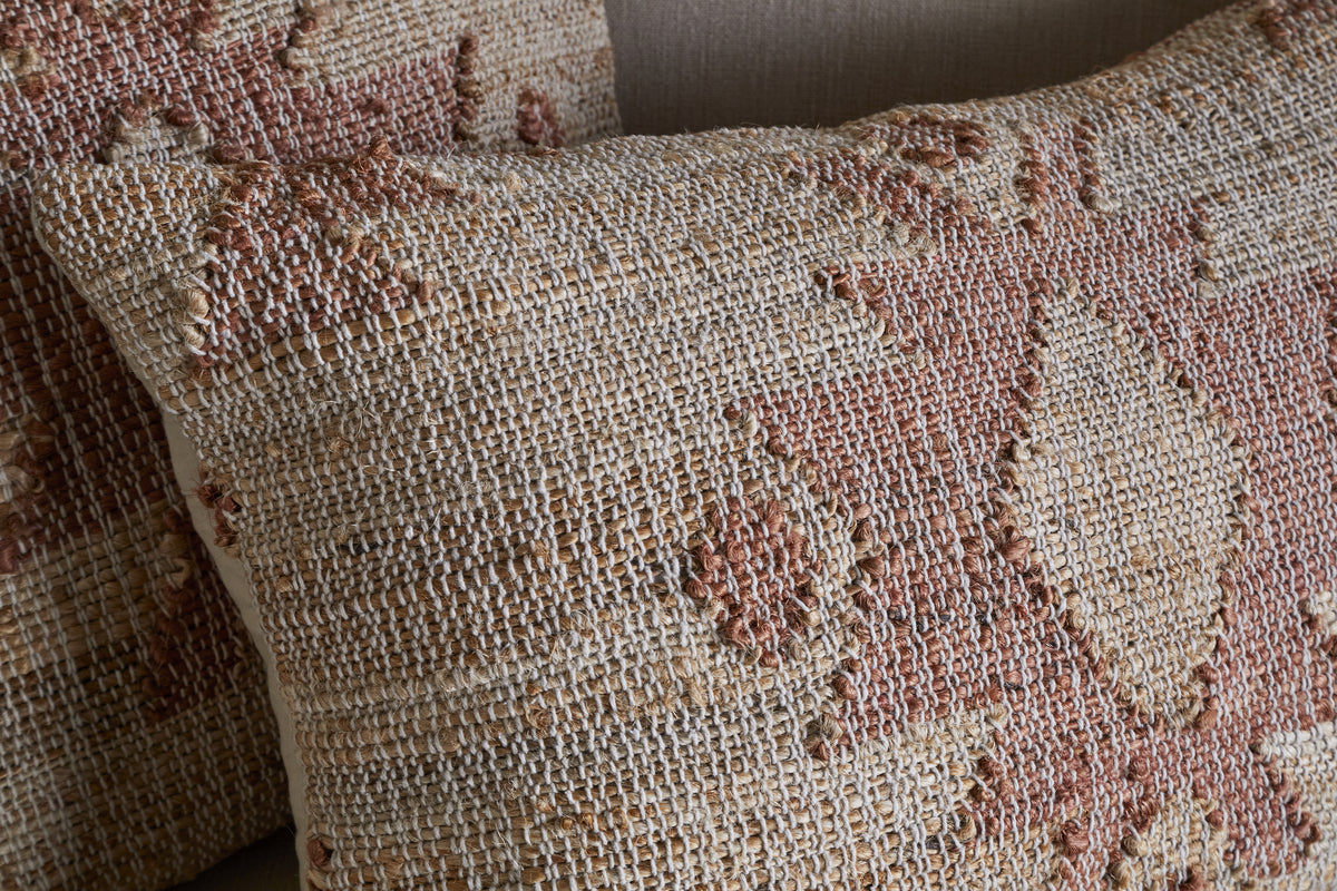 Close-up of two Nila Gul Cushion Covers by nkuku in earthy beige and rust, featuring woven geometric patterns and textured, raised stitching for a handcrafted, Indian-inspired look against a neutral background.