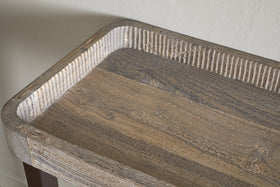 A close-up of the nkuku Nisha Reclaimed Wood & Iron Console Table – Natural highlights its rounded edges, grooved border, and distinctive weathered wood grain. The table is set against a light, subtly textured wall.