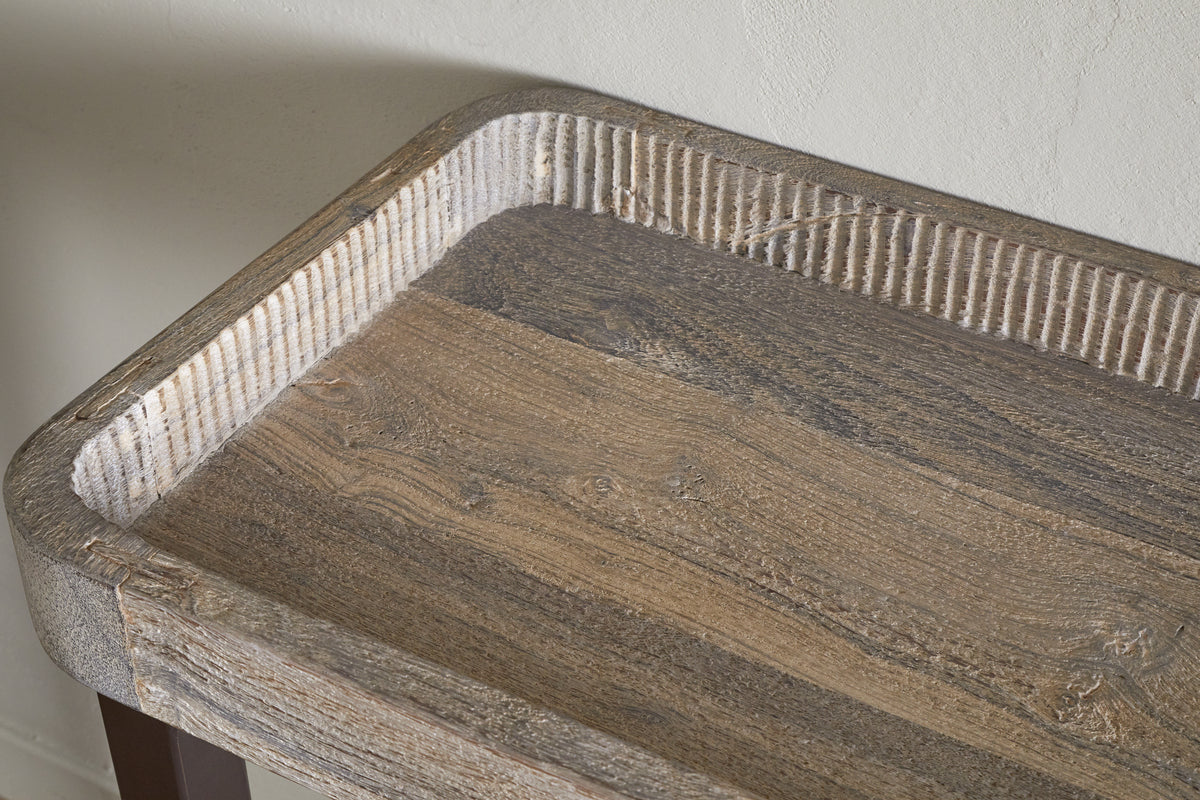 A close-up of the nkuku Nisha Reclaimed Wood & Iron Console Table – Natural highlights its rounded edges, grooved border, and distinctive weathered wood grain. The table is set against a light, subtly textured wall.