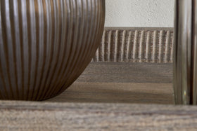 Close-up of a ribbed wooden tray on the nkuku Nisha Reclaimed Wood & Iron Console Table - Natural. A round brown vase and another container sit nearby, set against a light textured wall.