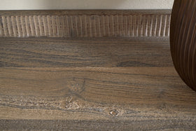 Close-up of the Nisha Reclaimed Wood & Iron Console Table by nkuku, showcasing its natural grain, knots, and textured ridges along the back. The light brown, weathered surface highlights its unique history; a rounded brown object is visible at the right edge.