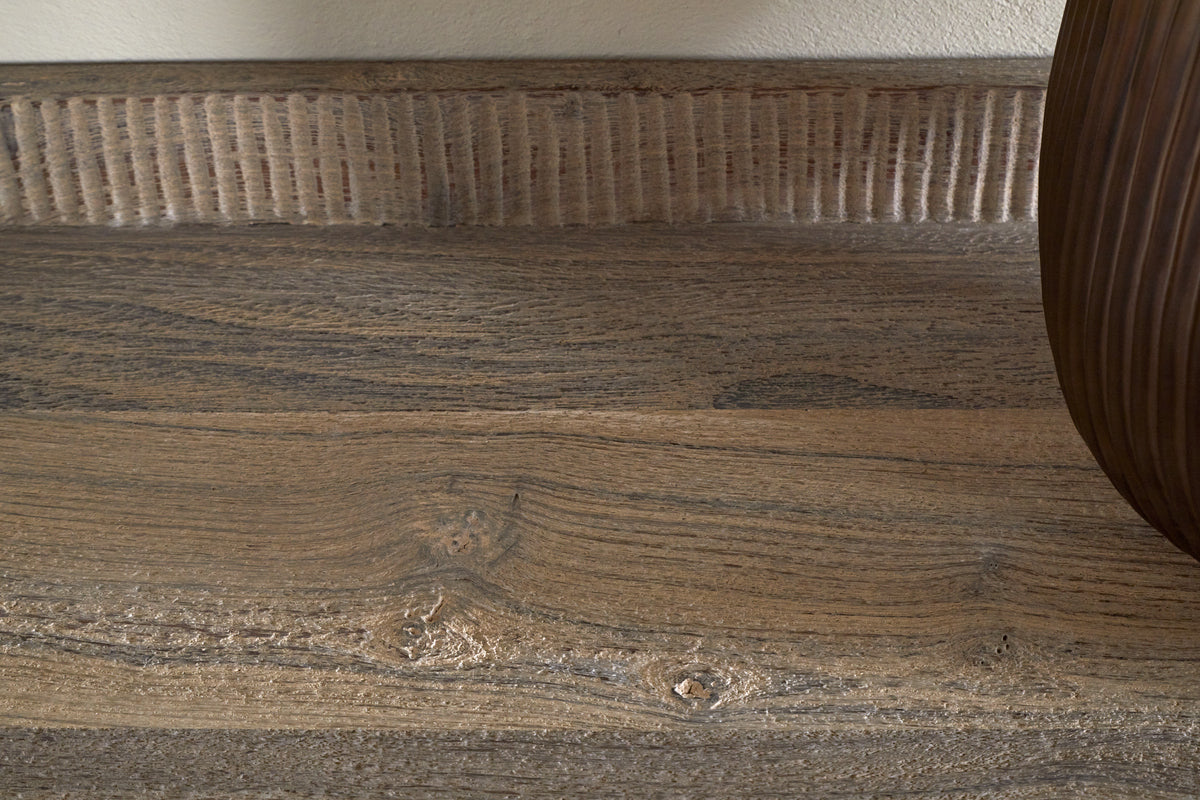 Close-up of the Nisha Reclaimed Wood & Iron Console Table by nkuku, showcasing its natural grain, knots, and textured ridges along the back. The light brown, weathered surface highlights its unique history; a rounded brown object is visible at the right edge.