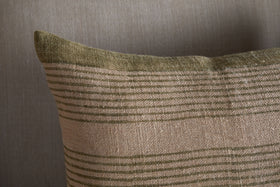 A close-up of the nkuku Eesha Jute Cushion Cover in Sage Green shows its block-printed horizontal stripes on beige jute, creating a cozy, modern rustic vibe. Only the upper left section is visible against a plain backdrop.
