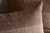 Close-up of nkuku's Eesha Jute Cushion Cover - Rust, featuring a modern rustic design with textured woven jute and horizontal cream stripes in the foreground. The background displays a solid brown pillow, both offering a cozy, natural look.
