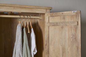 The Vivan Grooved Wardrobe - Natural by nkuku, shown open against a gray wall, displays three garments—a gray sweater, green shirt, and white shirt—on wooden hangers. Its light wood finish makes it perfect for stylish bedroom storage.