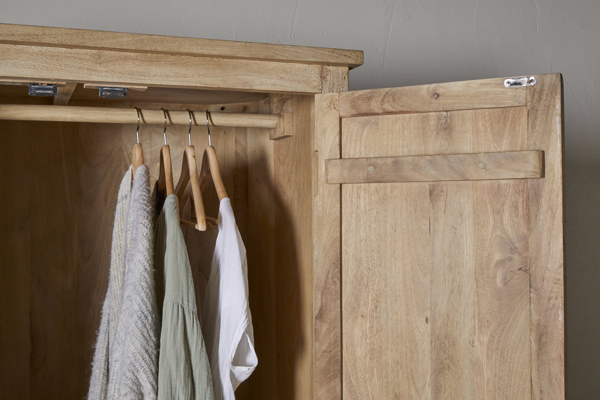 The Vivan Grooved Wardrobe - Natural by nkuku, shown open against a gray wall, displays three garments—a gray sweater, green shirt, and white shirt—on wooden hangers. Its light wood finish makes it perfect for stylish bedroom storage.