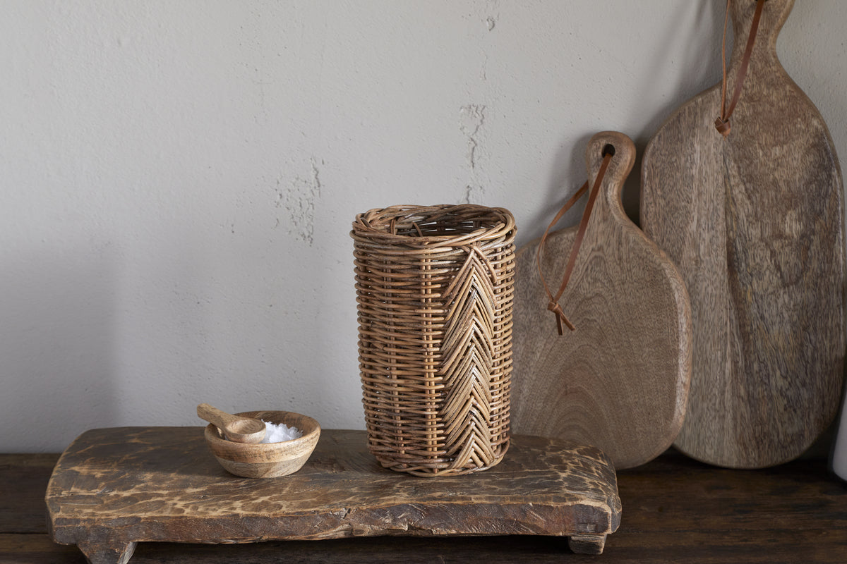 The Bersama Rattan Utensil Holder by nkuku features handwoven rattan on a wooden board, offering stylish kitchen storage.