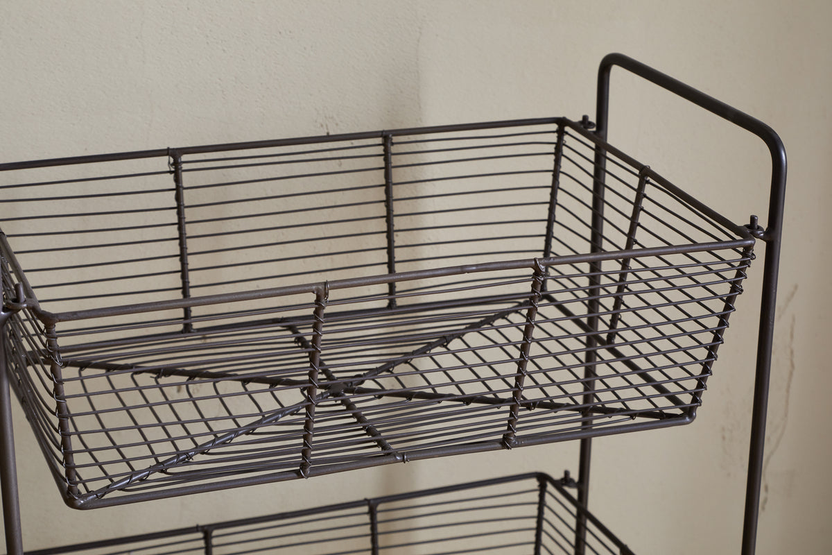 A close-up of the nkuku Inkollu Three Tier Storage Stand in antiqued brass, ideal for kitchen storage. The top rectangular basket displays its crisscross wire design, with another empty basket partially visible beneath.
