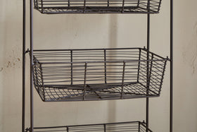 A close-up of the Inkollu Three Tier Storage Stand by nkuku in antiqued brass, featuring two empty rectangular wire baskets with a grid pattern—ideal for kitchen storage—set against a beige textured wall.