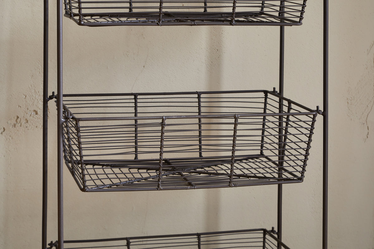 A close-up of the Inkollu Three Tier Storage Stand by nkuku in antiqued brass, featuring two empty rectangular wire baskets with a grid pattern—ideal for kitchen storage—set against a beige textured wall.