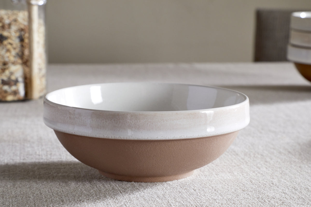 The nkuku Edo Dinnerware Set - Terracotta (Set of 12) features a ceramic bowl with a matte brown base and glossy off-white rim, styled on a beige tablecloth for an elegant, minimalist look in your tableware collection.