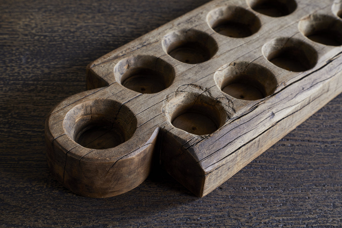 The Makala Reclaimed Wood Tealight Holder by nkuku features carved pits and a large well, crafted from weathered wood for a unique, cultural accent—perfect as a striking decorative piece for your home.