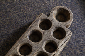 A close-up of the nkuku Makala Reclaimed Wood Tealight Holder - Natural, featuring six round tealight slots and one larger holder with visible wood grain and cracks, perfect as a rustic home decor accent on a dark textured surface.