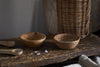The nkuku Daruka Salt & Pepper Dipping Bowls with Spoons - Natural are shown on a rustic surface beside coarse salt, with a wicker basket and beige cloth nearby—ideal for serving condiments stylishly.