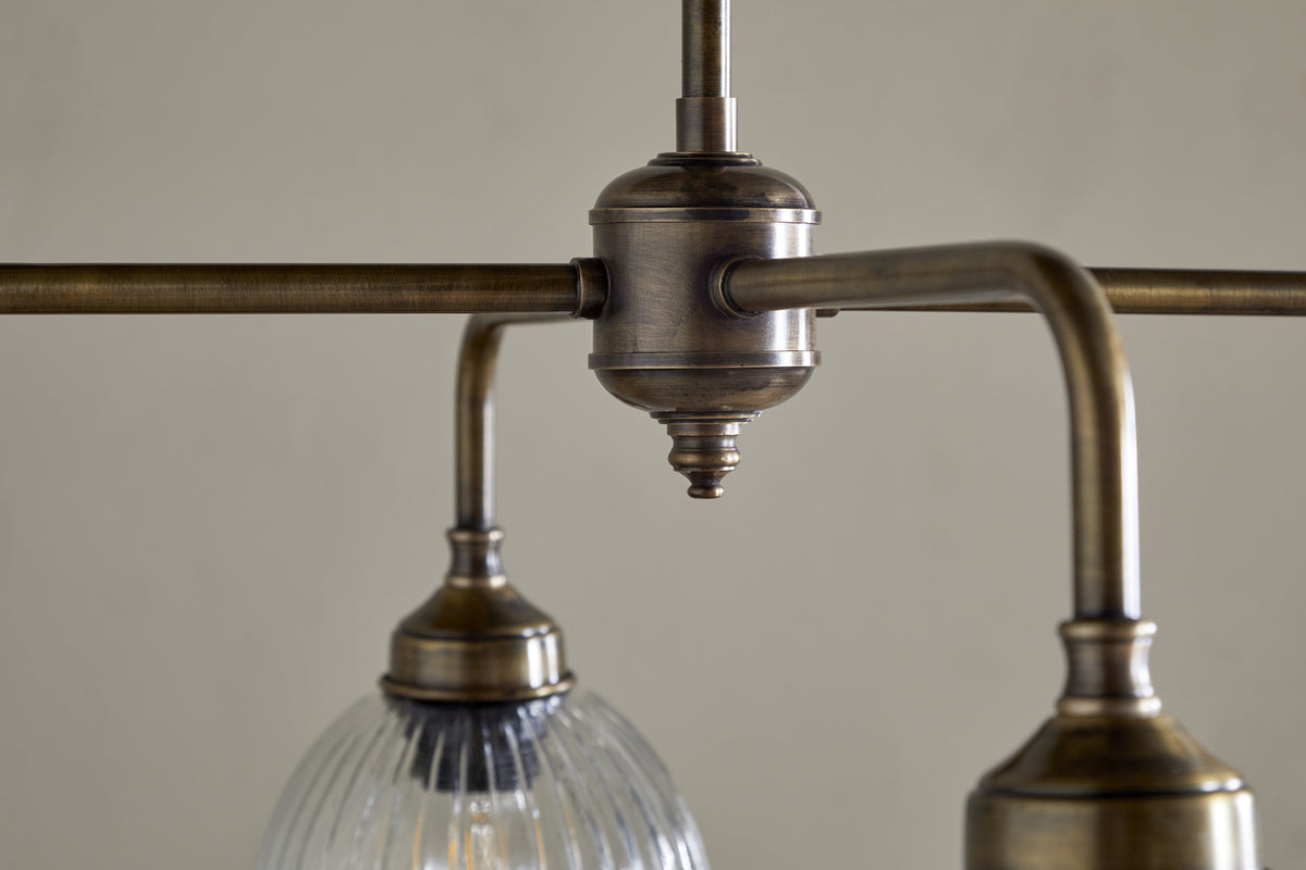 Close-up of the nkuku Kakira Chandelier Pendant in Antique Brass & Clear, featuring two downward arms—one with a ribbed glass shade—and an aged brass finish for classic charm, shown against a plain background.