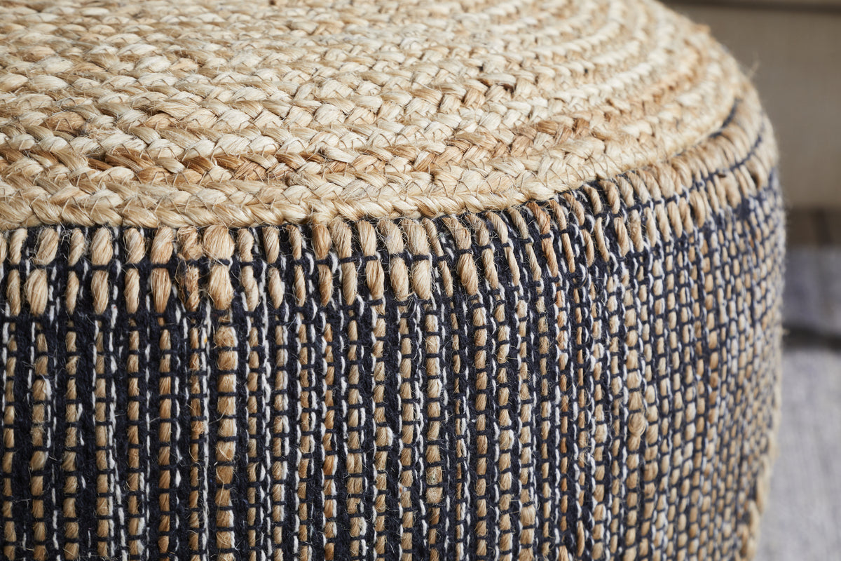 Close-up of the Kapil Jute Round Pouf - Charcoal by nkuku, featuring a braided jute top and textured sides with vertical charcoal threads. The detailed handwoven design highlights its artisan look, adding a stylish accent to any room.