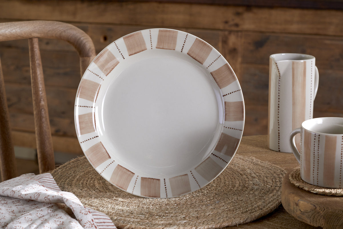 The Patthar Dinnerware Set by nkuku, featuring cream and clay tones with a beige and brown geometric border, adds rustic charm to your table. The 12-piece set sits atop a woven placemat, completed by matching mug and creamer.