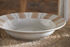 The Patthar Pasta Bowl - Cream & Clay by nkuku, with beige brushstroke patterns and dotted rim, rests on a woven placemat. A matching dish appears at the edge, highlighting the rustic, handcrafted charm of this dinnerware collection.