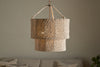 The Thimba Woven Jute Chandelier by nkuku, featuring a double-layered natural jute design, hangs above a neutral couch with pillows, casting a soft glow and rustic texture from matching woven cords.