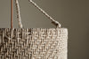 Close-up of the Thimba Woven Jute Chandelier by nkuku, showcasing its rustic texture, zig-zag pattern, and thick rope handle threaded through a metal ring. Set against a neutral beige background with gentle natural light.