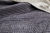 A close-up of the textured Nidra Velvet & Linen Bed Quilt in charcoal by nkuku, layered over a ribbed gray blanket. The soft, cozy Kantha-quilted fabric is ideal for King and Super King beds.