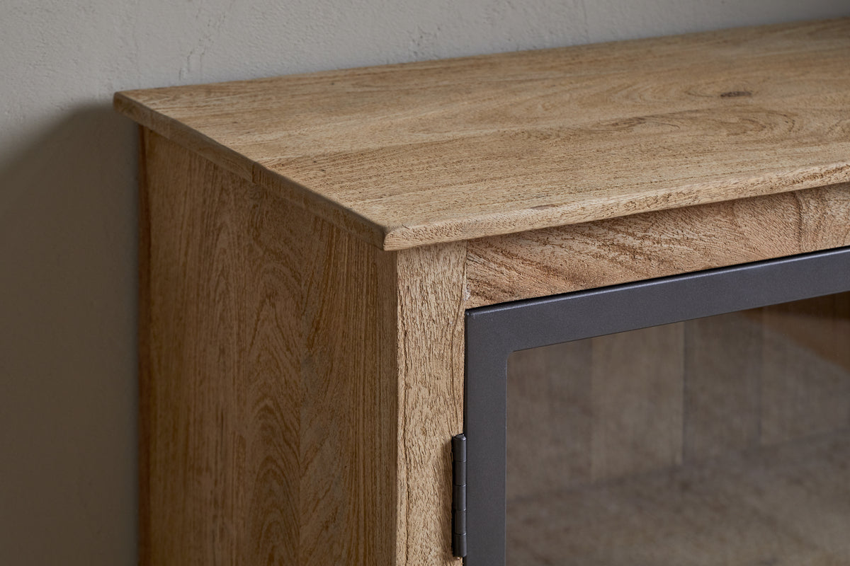 Close-up of the Nirvi Mango Wood & Iron Sideboard - Black by nkuku, showing the glass door with a black metal frame, set against a light wall.