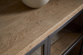 Close-up of the Nirvi Mango Wood & Iron Sideboard by nkuku, showcasing its natural mango wood grain, modern black iron edges, and legs—blending industrial style with rustic charm. Ceramic bowl displayed on top.