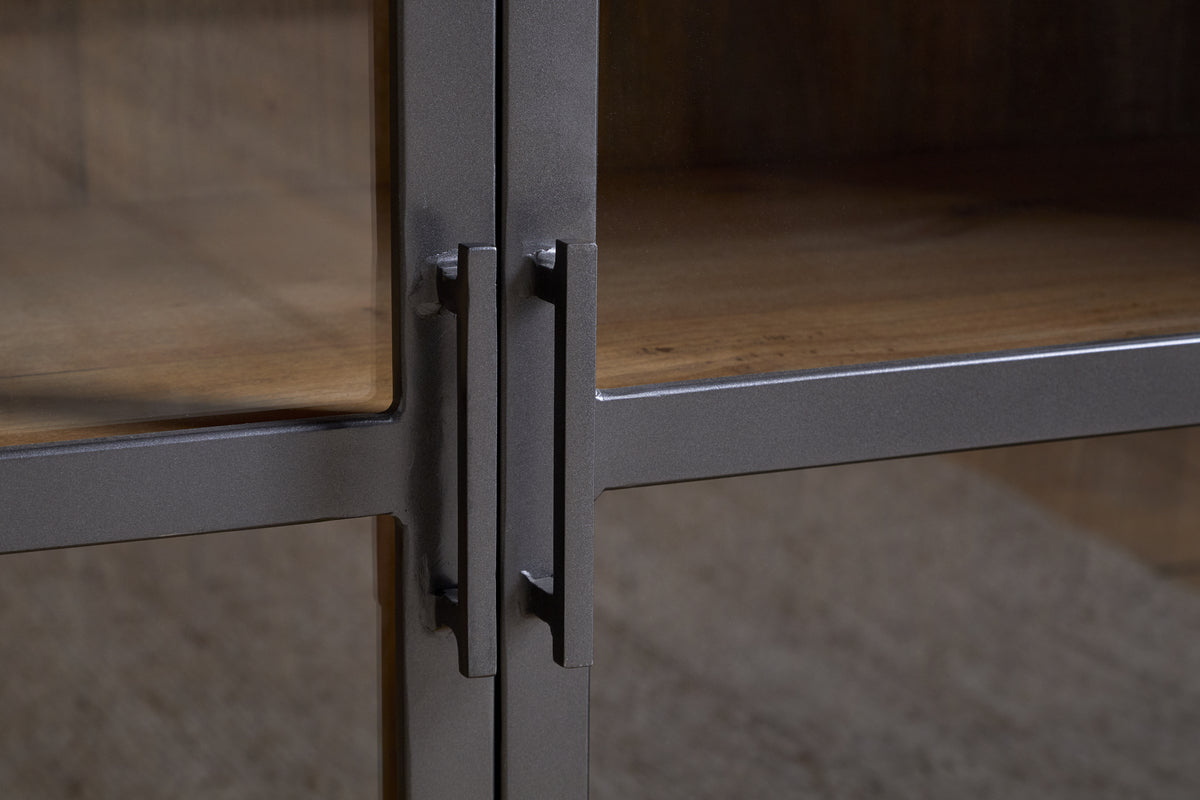 Close-up of two black metal handles on the glass cabinet doors of the nkuku Nirvi Mango Wood & Iron Sideboard - Black, showcasing the detailed texture of its iron and mango wood surfaces and wooden interior shelves.