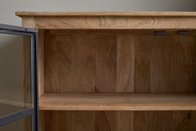 A close-up of the nkuku Nirvi Mango Wood & Iron Sideboard in black, featuring an empty single shelf and a partially open glass door that highlights the natural grain and texture of mango wood.