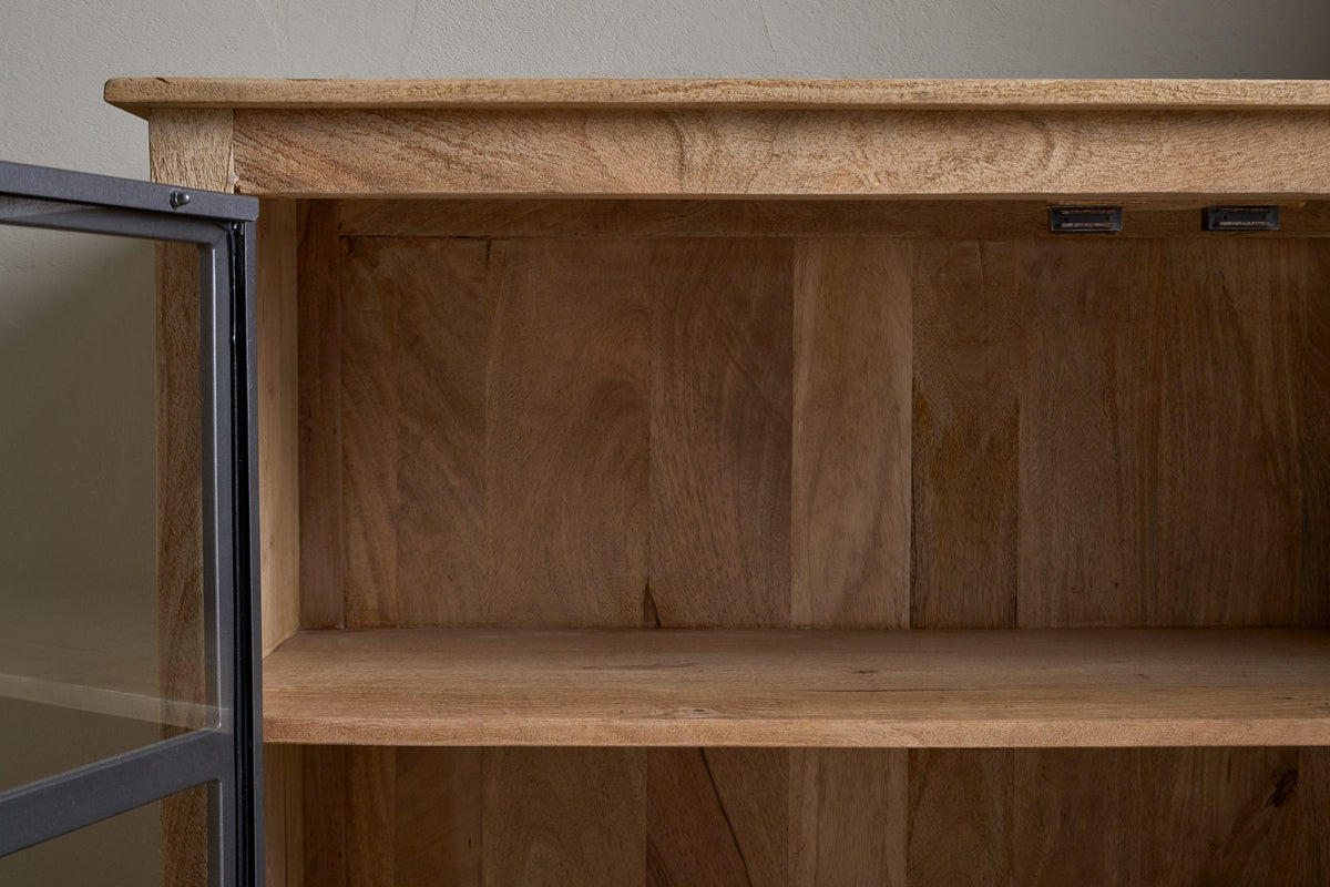 A close-up of the nkuku Nirvi Mango Wood & Iron Sideboard in black, featuring an empty single shelf and a partially open glass door that highlights the natural grain and texture of mango wood.