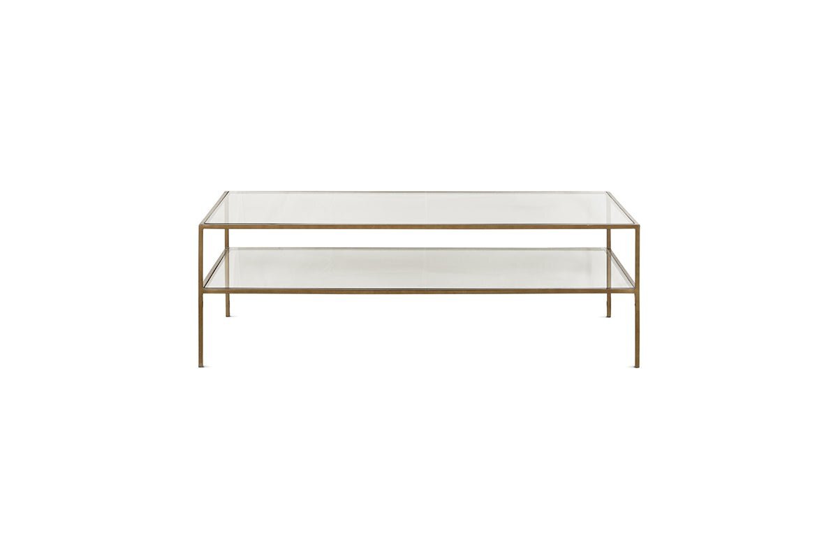 The Nakuru Iron & Glass Coffee Table by nkuku features a modern rectangular design with a slim gold metal frame, two clear glass surfaces (a top and lower shelf), and four slender legs, shown against a plain white background.
