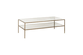 The nkuku Nakuru Iron & Glass Coffee Table features a rectangular, two-tiered design with a brass-finished iron frame and clear glass shelves, offering an elegant look ideal for modern spaces. Shown angled on a white background.