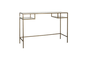The Nakuru Iron & Glass Console Table by nkuku features a slender metallic gold frame and clear glass top, with two lower glass shelves. Its spaced legs and brass finish give it an airy, modern style—ideal as a hallway console table.