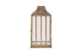 The nkuku Nampo Lantern - Aged Antique features a weathered brass finish, rectangular shape, glass panels on all sides, and vertical front metal bars. It has a flat top with handle and is shown against a plain white background.