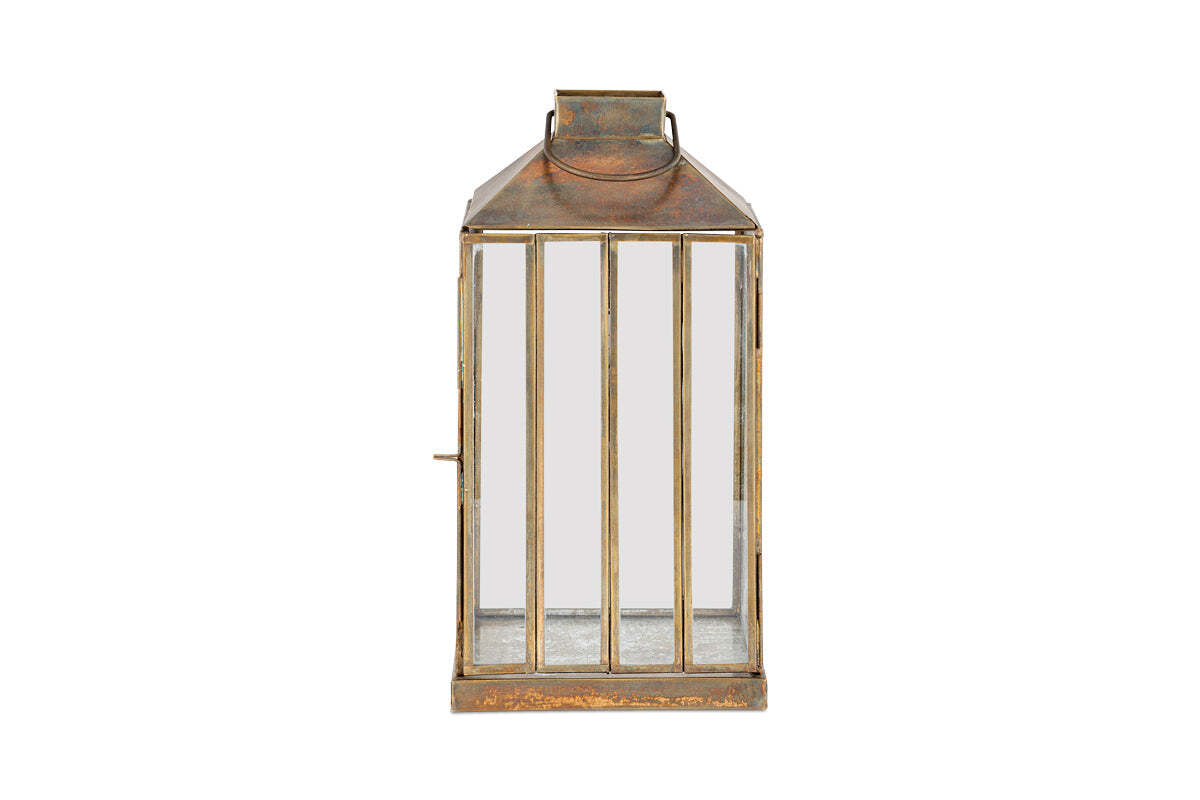 The nkuku Nampo Lantern - Aged Antique features a weathered brass finish, rectangular shape, glass panels on all sides, and vertical front metal bars. It has a flat top with handle and is shown against a plain white background.