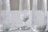 A set of four nkuku Otuba Champagne Flutes in clear glass is arranged on a light grey textured surface, with one flute sharply in focus at the center and the others partially visible on either side.