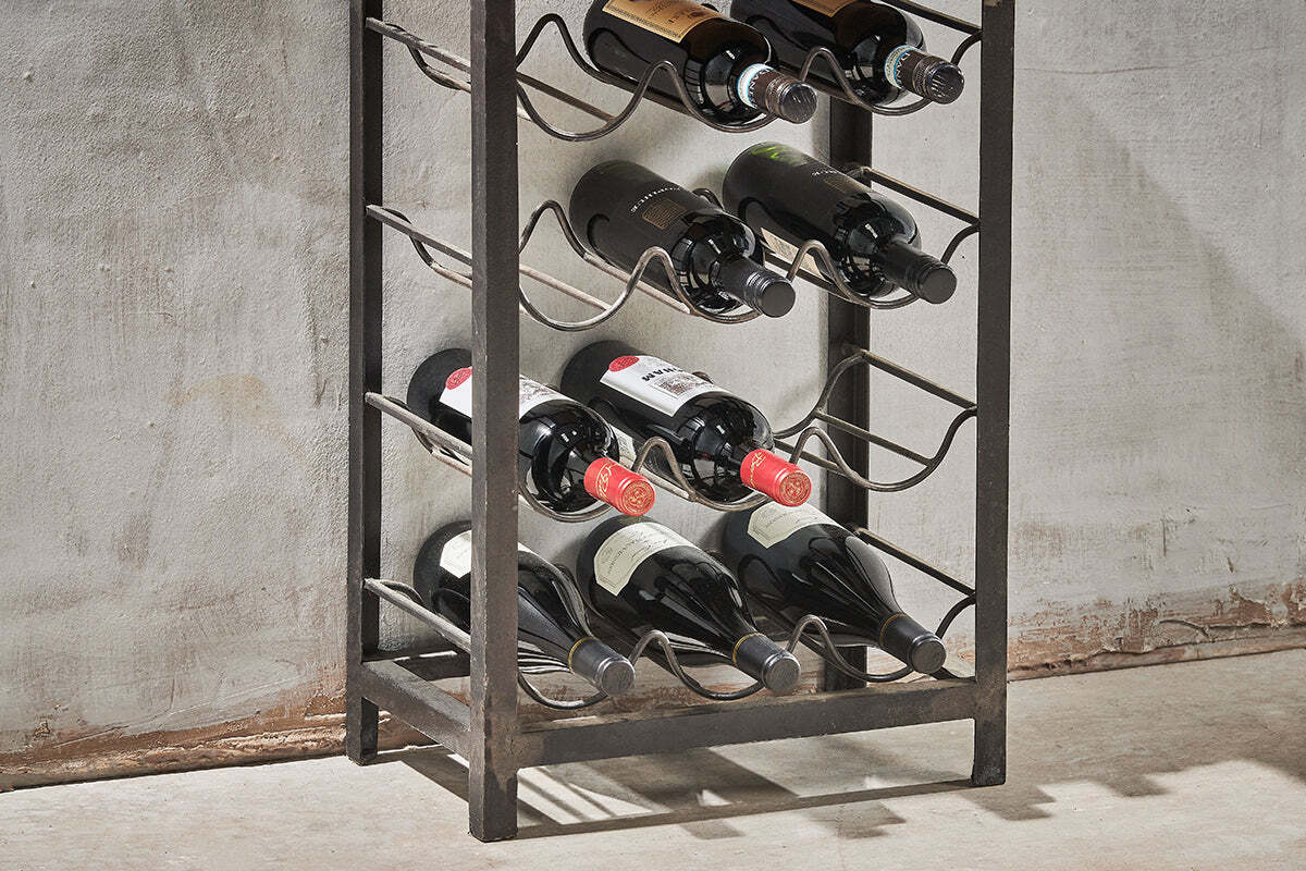 The nkuku Obra Industrial Wine Rack (Small), crafted from mango wood and iron, displays up to ten bottles horizontally. Its rustic black finish and open sides pair stylishly with the textured wall backdrop; most bottles show dark glass and clear labels.