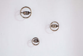 Three Olani Bathroom Hooks by nkuku in antique brass are mounted on a plain white wall in a loose triangular formation, casting soft shadows and creating a subtle, spa-like ambiance.