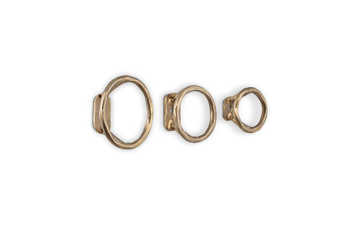 The nkuku Olani Bathroom Hooks - Antique Brass (Set of 3) feature handcrafted, unevenly textured metal rings in varying sizes, adding an organic, spa-inspired accent to your bathroom décor.