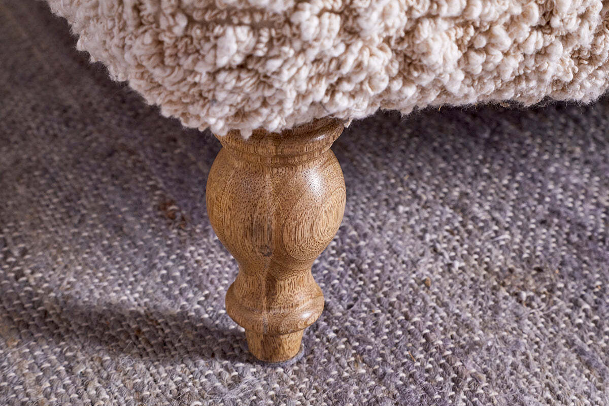 Close-up of a turned oak leg beneath nkuku’s Otas Teddy Ottoman - Off White. The cream boucle upholstery and textured grey rug accentuate the ottoman’s elegant, rounded form.
