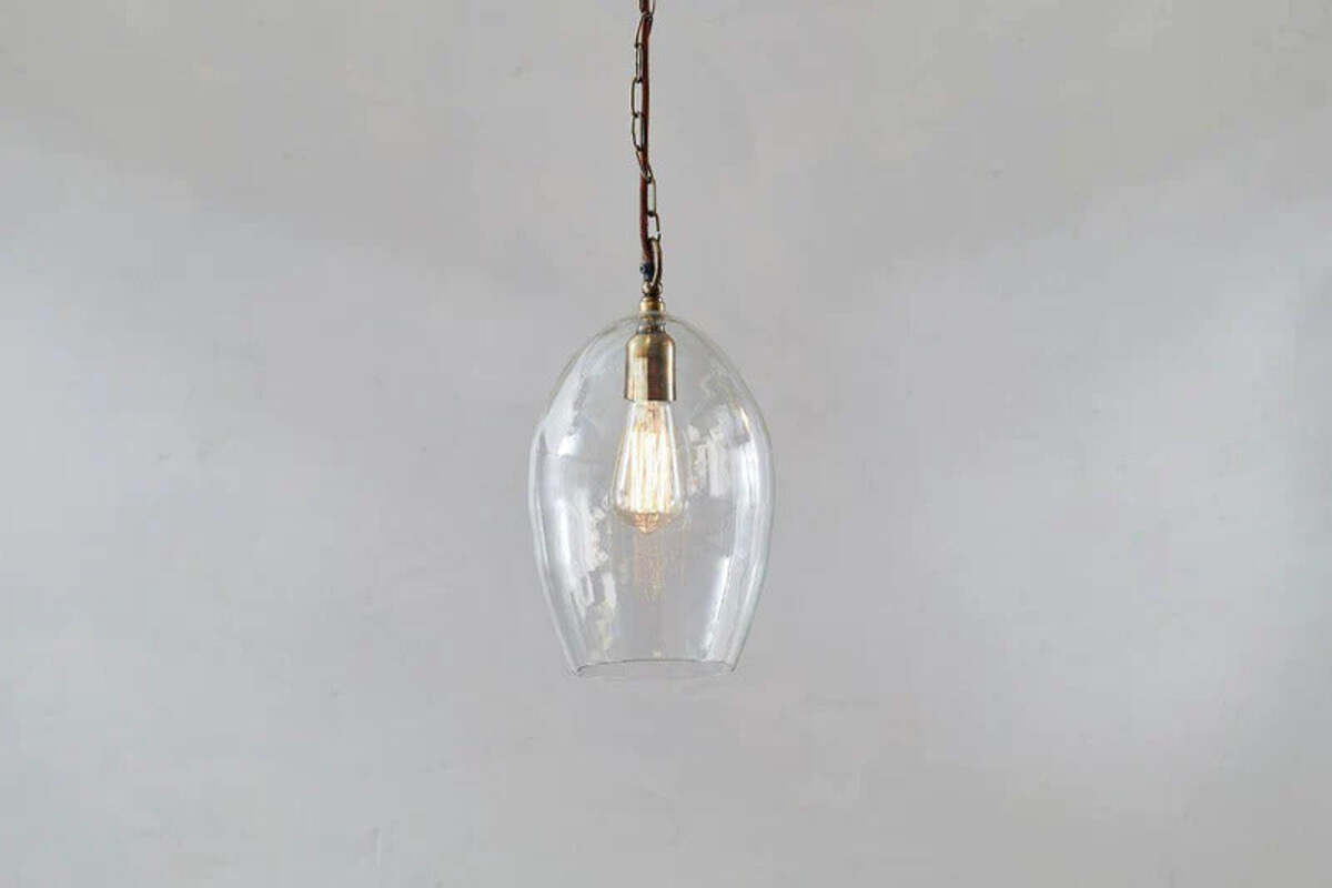 The Otoro Recycled Glass Pendant - Clear - Small Oval by nkuku features a dome-shaped glass shade and brass fittings with a vintage-style exposed bulb, making it a stylish, minimalist lighting choice.